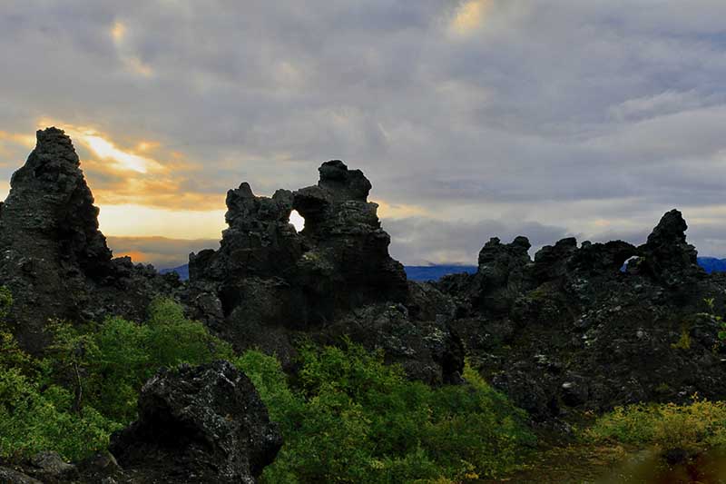 Sunlit lava formations at Dimmuborgir, Iceland, with vibrant green moss and blood red sky ad dusk