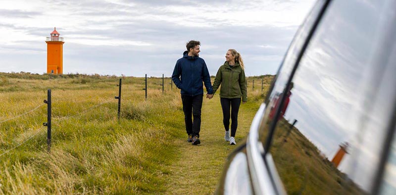 Couple on a rental car walking towards Hvalnesviti Lighhouse