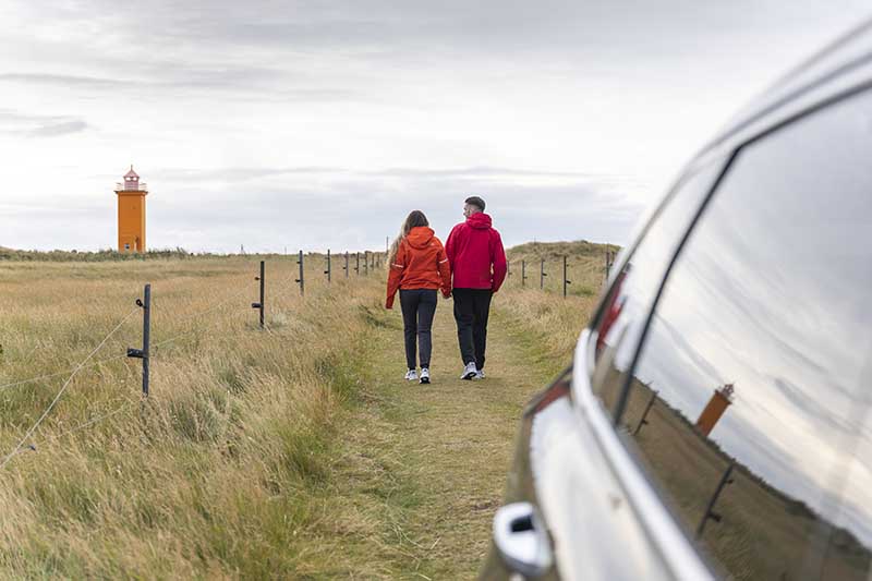Couple on a rental car walking towards Hvalnesviti Lighhouse