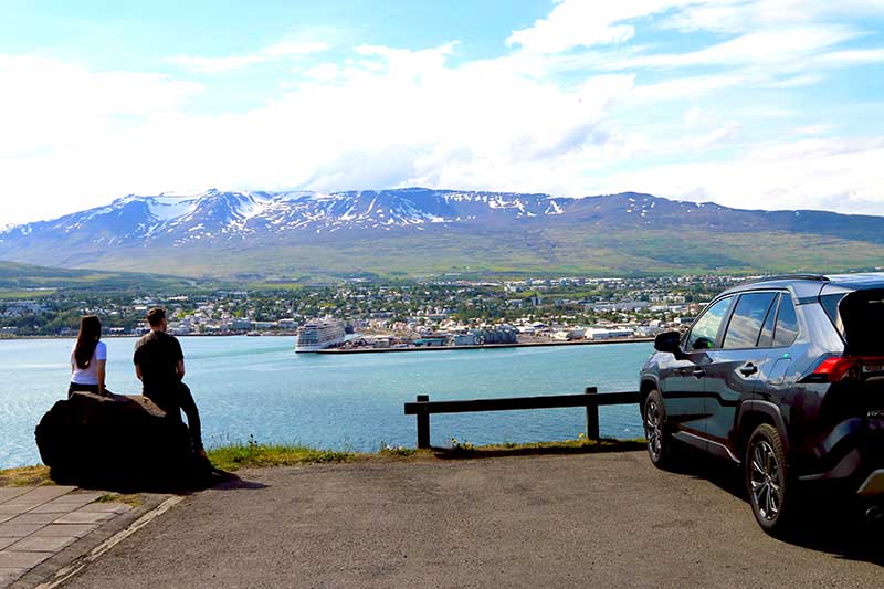 Couple with rental SUV overlooking the bautiful town of Akureyri in Northern Iceland