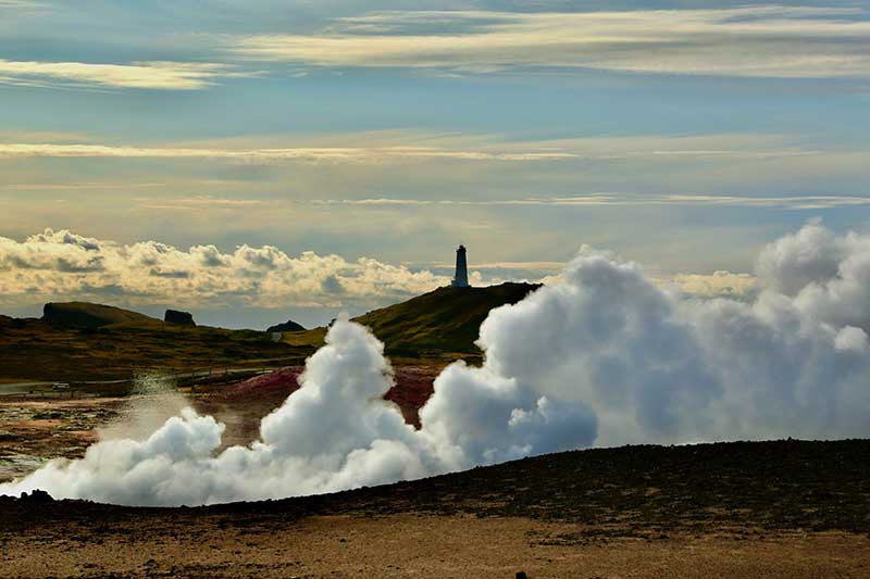 Lighthouse and geothermal steam rising on Reykjanes Peninsula.